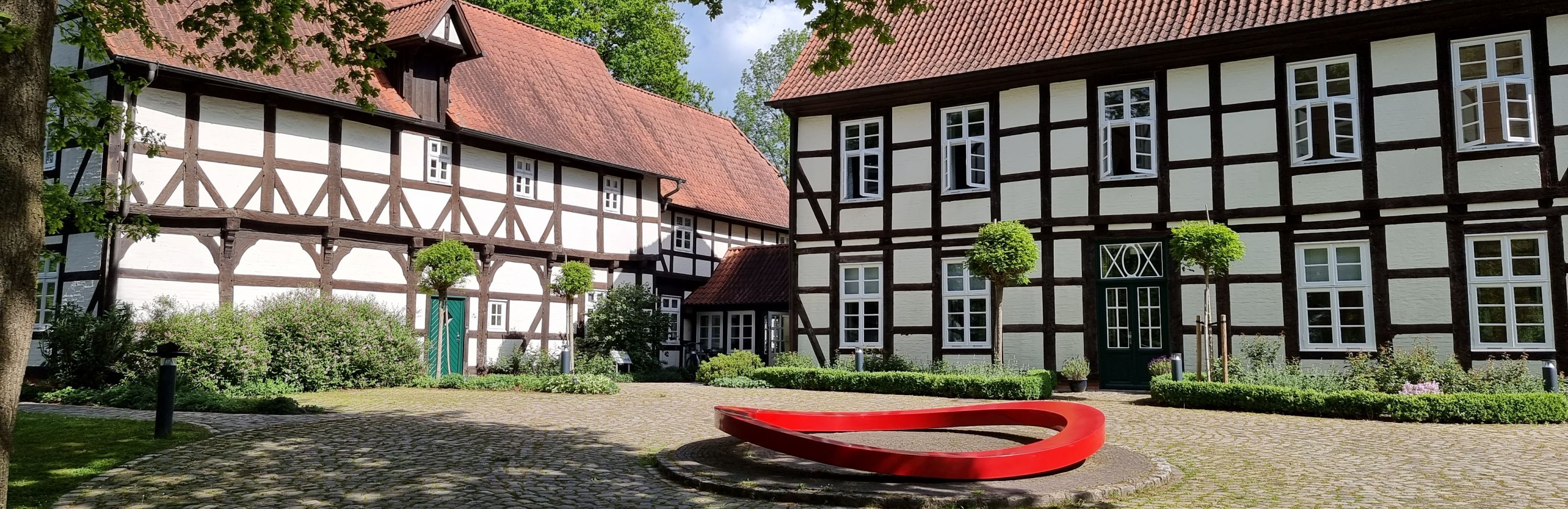 Die Freudenburg: Fachwerkhäuser um einen gepflsterten Hof gruppiert. In der Mitte eine Kunstskulptur: ein großer, roter Stahlring.